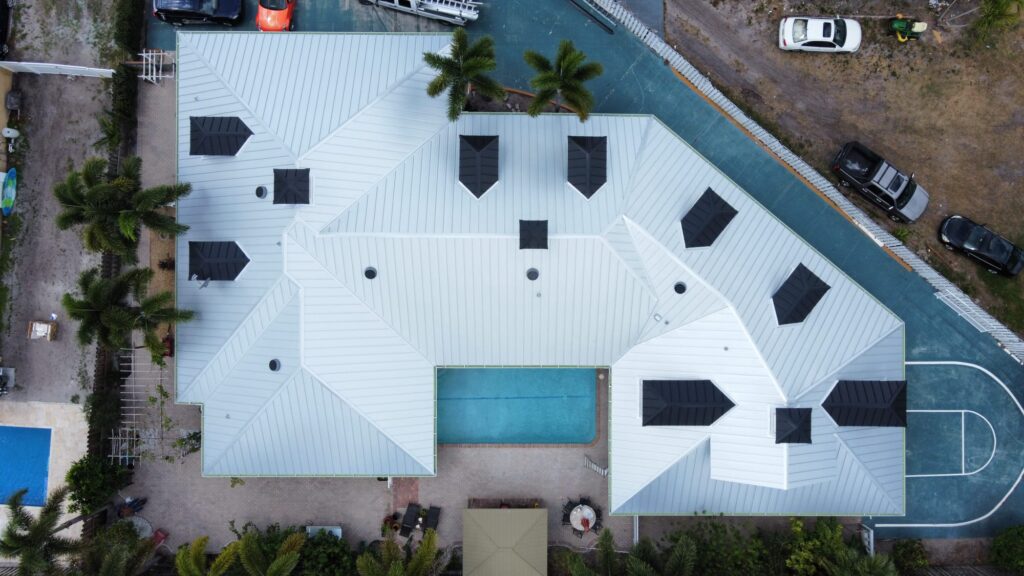 Aerial view of a large white metal roof with multiple dormers, pool, and basketball court in Greenacres, Florida